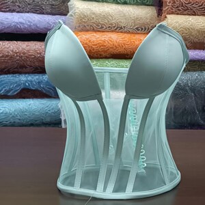 May include: A light blue mesh corset with a satin-like finish. The corset has a V-shaped neckline and a boned structure.