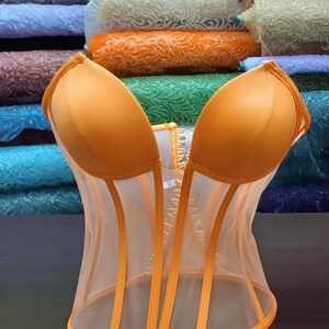 May include: A bright orange mesh corset with boning and a busk closure. The corset has a satin-like finish and is made of a sheer fabric.