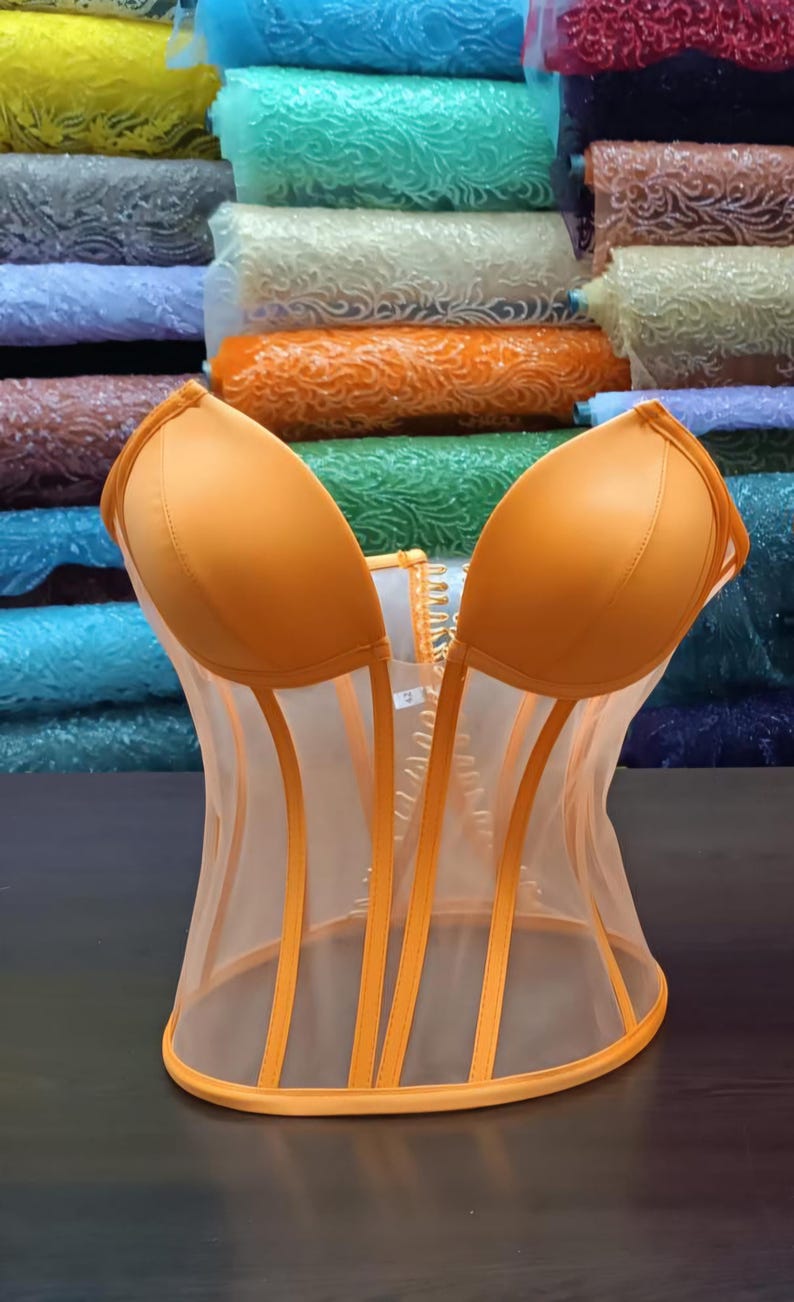 May include: A bright orange mesh corset with boning and a busk closure. The corset has a satin-like finish and is made of a sheer fabric.