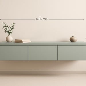 Puede incluir: Un mueble flotante verde salvia con tres puertas, de 148,5 cm de ancho y 30 cm de alto, con una profundidad de 40 cm. Está decorado con un pequeño jarrón con vegetación, una pila de libros y un pequeño jarrón marrón.