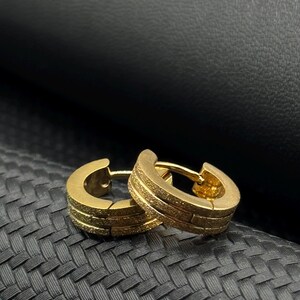 May include: A pair of gold hoop earrings with a textured finish. The earrings are made of metal and have a simple, modern design.