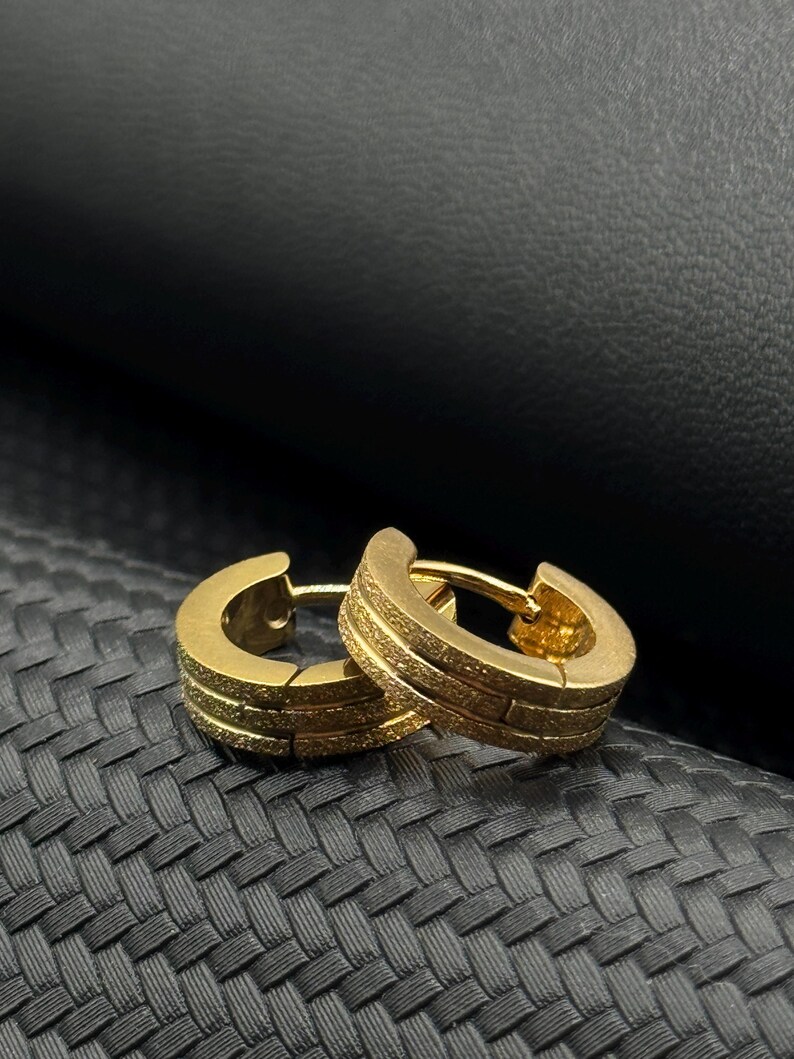 May include: A pair of gold hoop earrings with a textured finish. The earrings are made of metal and have a simple, modern design.