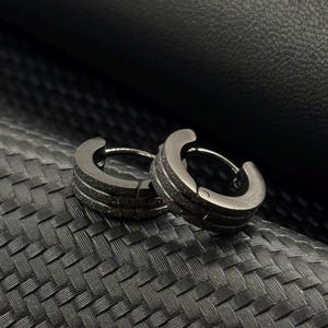 May include: A pair of black hoop earrings with a textured finish. The earrings are made of metal and have a simple, modern design.