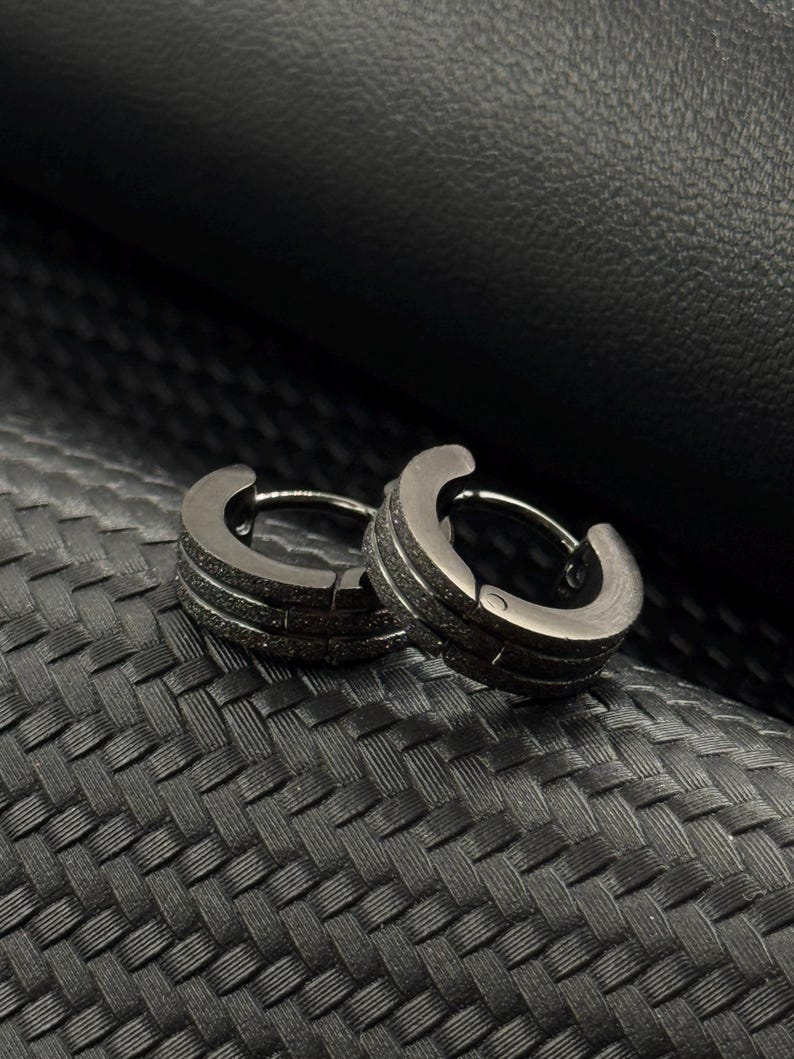 May include: A pair of black hoop earrings with a textured finish. The earrings are made of metal and have a simple, modern design.