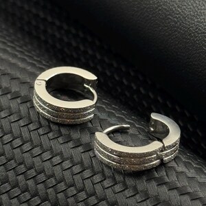 May include: A pair of silver hoop earrings with a row of small clear stones on each hoop.