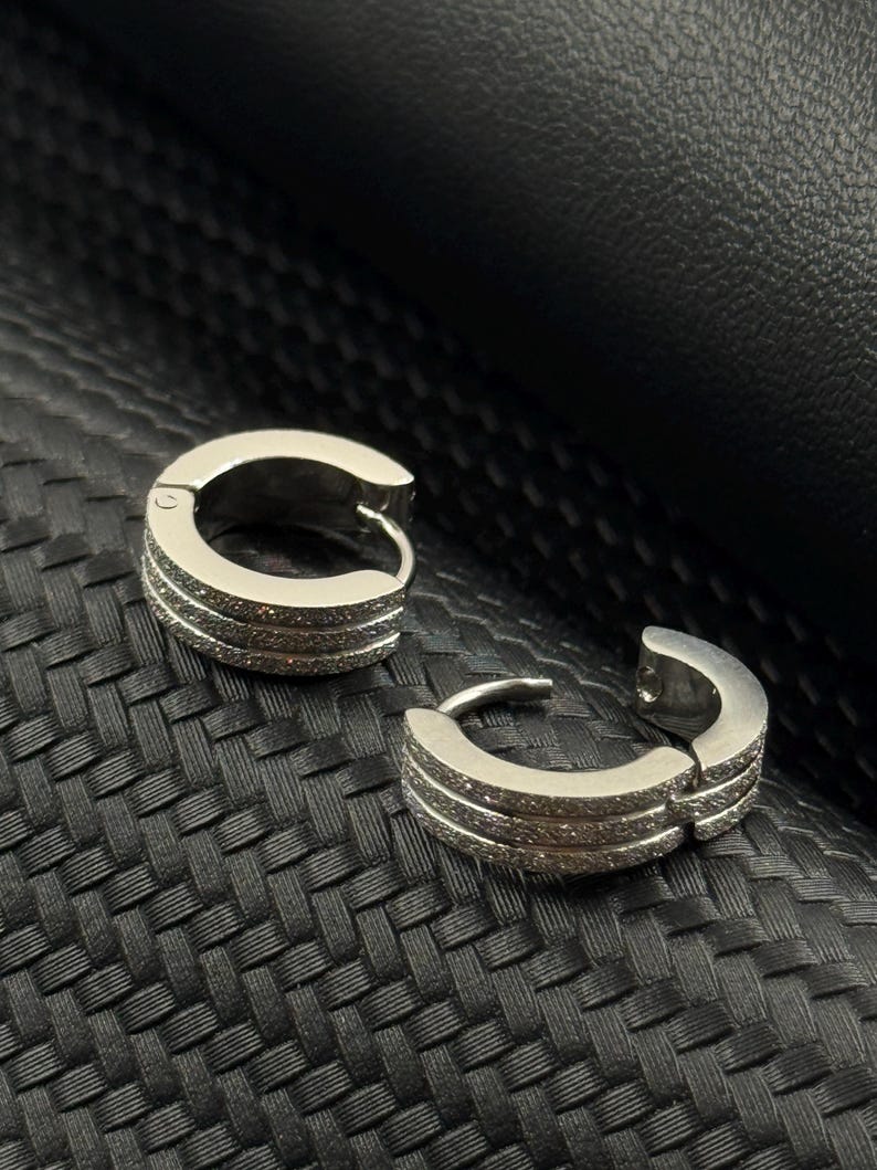 May include: A pair of silver hoop earrings with a row of small clear stones on each hoop.