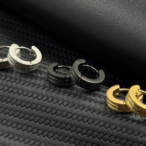 May include: Six hoop earrings in different finishes. Two silver, two black, and two gold hoop earrings.