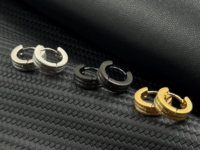 May include: Six hoop earrings in different finishes. Two silver, two black, and two gold hoop earrings.