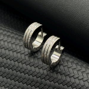 May include: A pair of silver hoop earrings with a textured, sparkly finish. The earrings are simple and elegant.