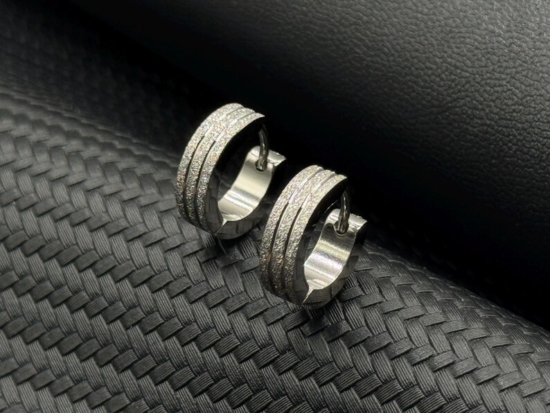 May include: A pair of silver hoop earrings with a textured, sparkly finish. The earrings are simple and elegant.