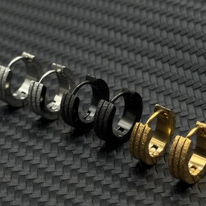May include: A set of six hoop earrings in different finishes, including silver, black, and gold. The earrings have a textured surface and are arranged in a row.