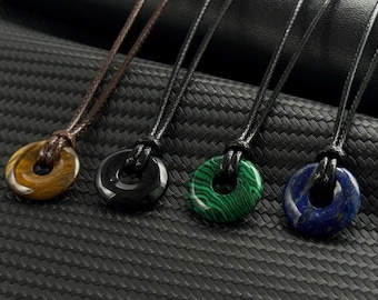 May include: Four stone pendant necklaces. The pendants are donut-shaped, with a tiger's eye, black onyx, green malachite, and blue lapis lazuli. Each pendant is strung on a black or brown cord.