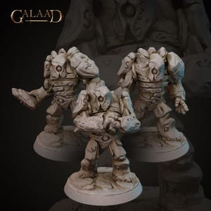 May include: Three stone-like figures with detailed armor and facial features. The figures are in various poses, with one raising a foot, another clenching fists, and the third standing upright. The figures are on a rocky base, with the word "Galaad" in the upper left corner.