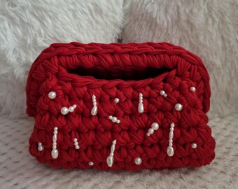 May include: A red, crocheted clutch with white pearl embellishments. The handmade bag features a rectangular shape with a wide opening. The pearls are arranged in a decorative pattern across the front of the bag.