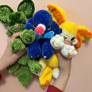 May include: A collection of handmade crochet plush toys in various colors. The toys include a green mouse, a blue penguin with a red beak, and a yellow and white rabbit. The toys are soft and fluffy, with detailed features.