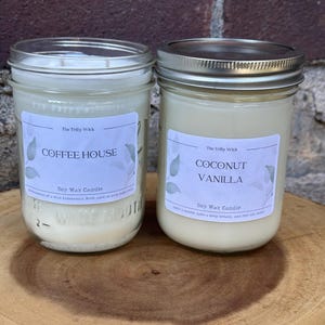 May include: Two glass jar soy wax candles with silver lids. The left candle label reads The Trilly Wick, COFFEE HOUSE, Soy Wax Candle. The right candle label reads The Trilly Wick, COCONUT VANILLA, Soy Wax Candle. Both jars feature white labels with green leaf illustrations.
