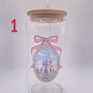 May include: A clear glass tumbler with a bamboo lid and a clear straw. The tumbler features a pink bow and an oval design with a castle illustration. The design is in pink, blue, and white.
