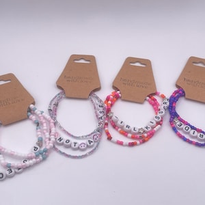 Può includere: Quattro braccialetti di perline fatti a mano nei toni del rosa, bianco e blu. Ogni braccialetto presenta una parola diversa scritta con perline di lettere bianche. Le parole sono: "TRANS", "NOT A", "IRL KISSER" e "PRIDE".