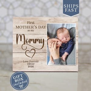 May include: Wooden photo frame with a picture of a baby and the text "First Mother's Day as my Mommy." The frame also includes the text "Love Forever Oliver 2026." A gift box is included.