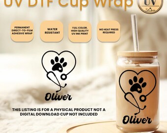 Op de afbeelding: Een heldere glazen beker met een bamboe deksel en rietje, met een zwart pootafdruk- en stethoscoopontwerp in een hart, met de naam "Oliver" eronder. De tekst "UV DTF Cup Wrap" staat bovenaan.