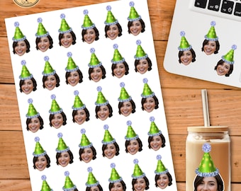 Op de afbeelding: Vel stickers met een lachende vrouw met een groene feesthoed met een blauwe pompon. De stickers staan op een witte achtergrond. Een laptop en een glas met een rietje staan op de achtergrond.