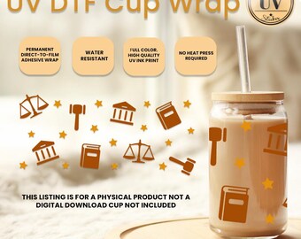 Op de afbeelding: Een transparante glazen beker met een bruin houten deksel en een rietje. De beker is versierd met een patroon van gouden sterren, weegschalen van de rechtvaardigheid, boeken en gebouwen. De tekst "UV DTF Cup Wrap" staat bovenaan de afbeelding. De tekst "This listing is for a physical product not a digital download cup not included" staat onderaan de afbeelding.