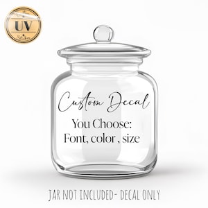 May include: A clear glass jar with a lid, featuring the text "Custom Decal" and "You Choose: Font, color, size." The jar is empty, and the text is in a stylish script font. A small sticker is in the upper left corner.