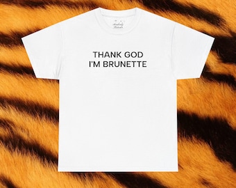 May include: White t-shirt with the text "THANK GOD I'M BRUNETTE" in black, centered on the front. The shirt is displayed against a background with a tiger stripe pattern in shades of orange and brown.
