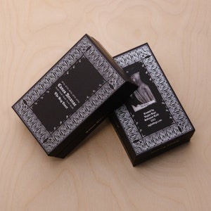 May include: Two black card decks with white ornate borders. The top deck has the text "Canes Arcanae The Way Tarot" on the front. The bottom deck has a black and white image of a person in a hooded robe.