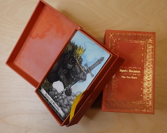 May include: A tarot card with a dinosaur wearing a crown and holding a sword. The card is called "Queen of Swords" and is from the "Ignis Arcanae: The Fire Tarot" deck.