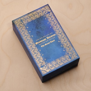 May include: A blue box with gold lettering that reads "Oceanum Arcanae The Ocean Tarot".