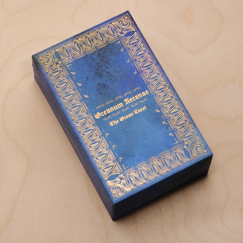 May include: A blue box with gold lettering that reads "Oceanum Arcanae The Ocean Tarot".
