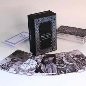 May include: A black box with silver lettering that reads "Canes Arcanae The Dog Tarot". The box is open and shows a deck of tarot cards with black and white illustrations of dogs.
