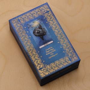 May include: A blue box with gold trim and a tarot card image of a fish with the text "The Sun" and "Created by Taylor Brynn Mulvaine-Todd 2021 taylorbrynn.com".