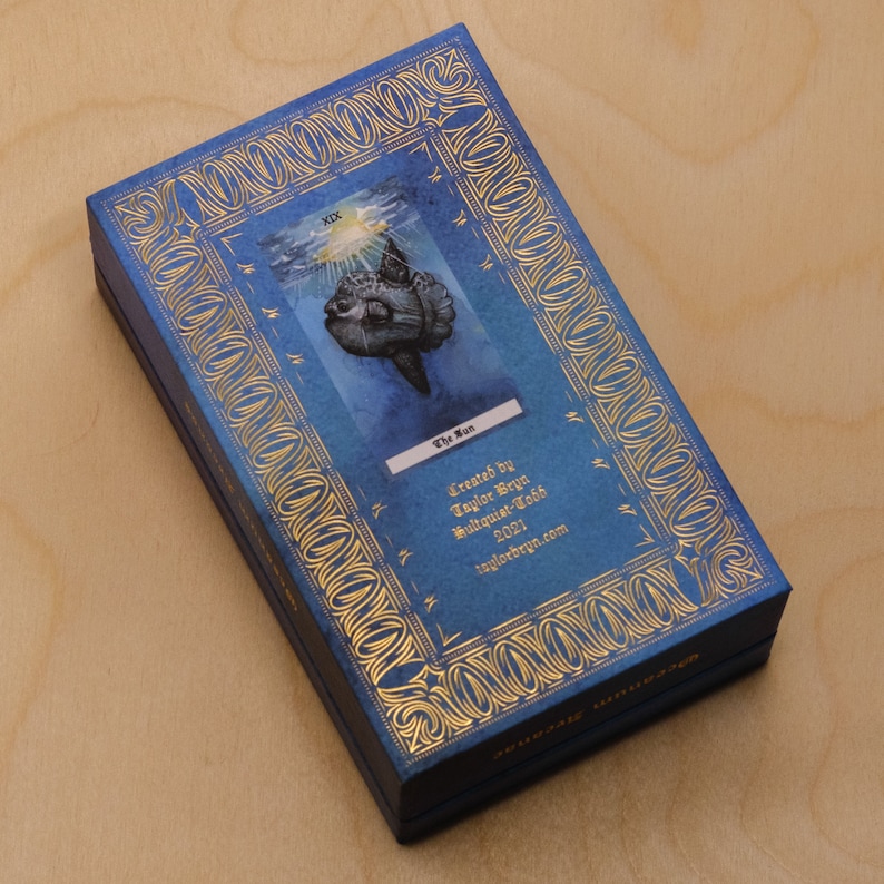 May include: A blue box with gold trim and a tarot card image of a fish with the text "The Sun" and "Created by Taylor Brynn Mulvaine-Todd 2021 taylorbrynn.com".