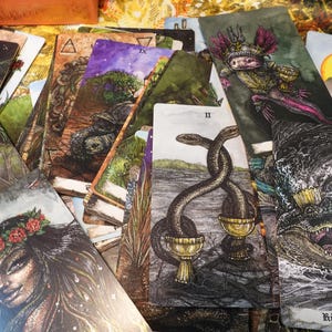 May include: A tarot card deck with a variety of cards spread out, including the King of Cups, the Two of Cups, and the Nine of Swords. The cards feature detailed illustrations with a dark and mystical aesthetic.