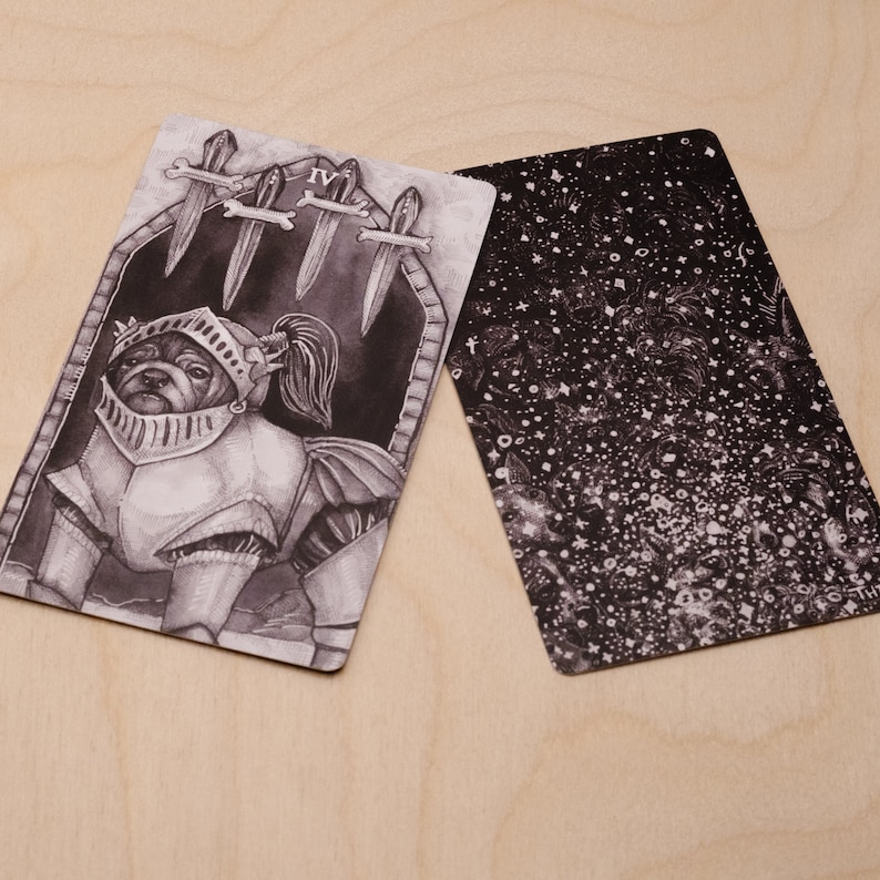 May include: A black and white tarot card with a dog wearing armor and a sword in its mouth. The card is labeled "IV" and has a black and white background with a pattern of stars.