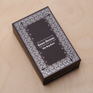May include: A black box with a white border and the text "Canes Arcanae The Dog Tarot" on the front.