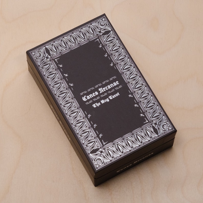 May include: A black box with a white border and the text "Canes Arcanae The Dog Tarot" on the front.
