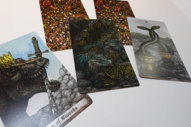 May include: Four tarot cards, each with a different illustration. The first card shows a green and brown lizard with a sword through its head. The second card shows a green and brown lizard with gold coins. The third card shows a green and brown lizard with gold coins. The fourth card shows two snakes intertwined with gold coins.