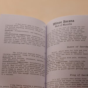 May include: Two pages from a book about tarot cards. The left page features a black and white illustration of a dog with the text "A dog turns away to wonder..." and "The solid-coat English Setter is a charming companion, ready to help you enjoy the good things in life." The right page features the text "Minor Arcana Suit of Swords" and "Wolves, which mate for life and live in family-like nuclear social groups, don't kindly to those who harm or threaten their young." The text "Queen of Swords" is also visible.