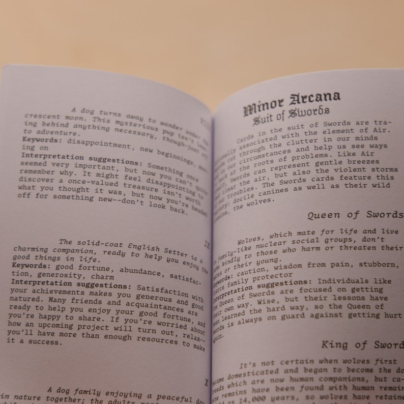 May include: Two pages from a book about tarot cards. The left page features a black and white illustration of a dog with the text "A dog turns away to wonder..." and "The solid-coat English Setter is a charming companion, ready to help you enjoy the good things in life." The right page features the text "Minor Arcana Suit of Swords" and "Wolves, which mate for life and live in family-like nuclear social groups, don't kindly to those who harm or threaten their young." The text "Queen of Swords" is also visible.