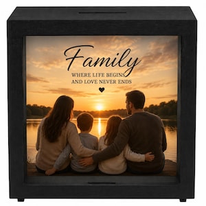 May include: A black wooden shadow box with a slot on top, featuring a sunset photograph of a family sitting on a dock. The text reads: Family WHERE LIFE BEGINS AND LOVE NEVER ENDS, with a small heart icon centered below the text.