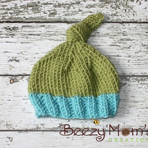 Puede incluir: Un gorro de bebé de punto verde y azul con un nudo en la parte superior. El gorro está hecho con un hilo suave y tiene un diseño sencillo.