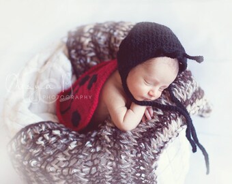 May include: A newborn baby wearing a red and black ladybug costume, sleeping on a brown and white knitted blanket.
