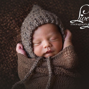 May include: A newborn baby wearing a brown knitted hat and a brown crocheted wrap, sleeping on a brown textured surface. The image includes the text "Live Loved Photography".