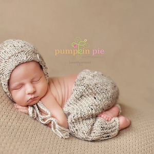 May include: A newborn baby wearing a knitted hat and matching trousers, sleeping on a textured beige background. The baby is wearing a beige knitted hat and matching trousers. The text "pumpkin pie" is visible in the image.