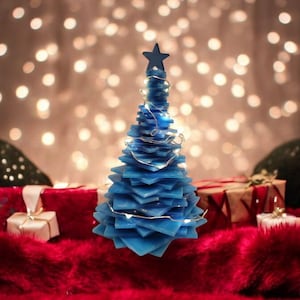 May include: A blue, layered Christmas tree decoration with a star on top, illuminated by fairy lights. The tree sits on a red surface with wrapped gifts and small decorative trees in the background. The background has a bokeh effect.