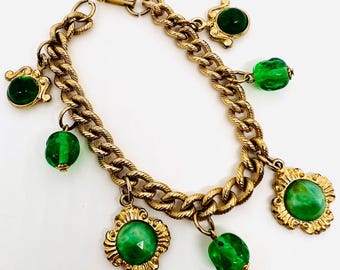 May include: A gold chain bracelet with multiple green glass charms. The charms are round, oval, and square shaped. The bracelet has a lobster claw clasp.