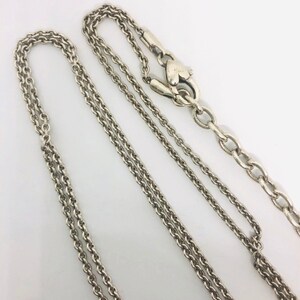 May include: Two silver chains with a heart-shaped clasp. The chains are of different lengths and thicknesses.